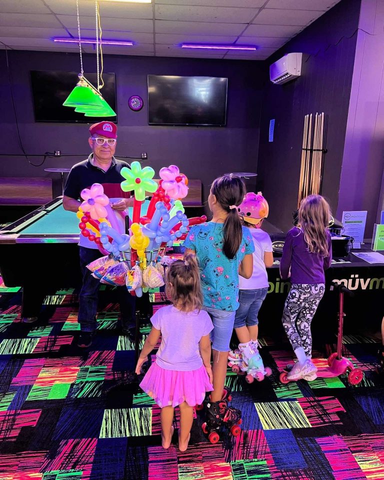 Children on roller skates gathered around a balloon-animal stand at an SSA community event.