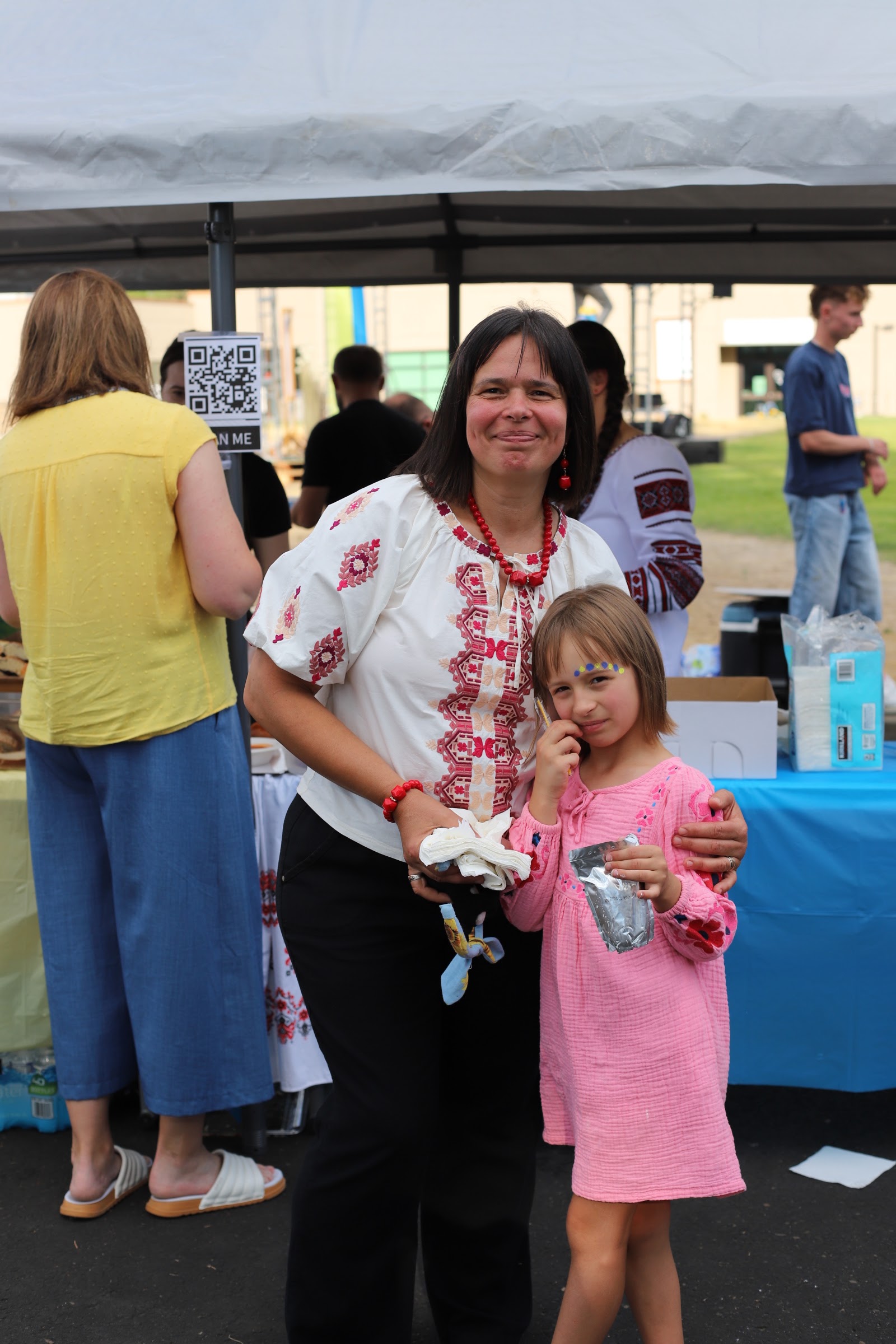 A woman and a girl wearing traditional embroidered Ukrainian vyshyvanka blouses at UA Fest, with another woman in traditional dress in the background.